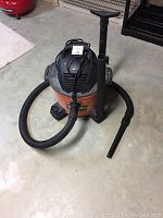 Photo showing the Rigid 6 gallon shop vacuum with black hose, extension wand attached, crevice tool, and flat nozzle attachments placed on concrete floor.
