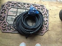 Coiled black porous Miracle-Gro soaker hose placed on a metal patterned mat, showing length and condition.