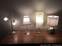 Four accent lamps on a wooden table showing varying styles and lit bulbs.