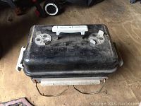 Full view of the closed portable Weber charcoal grill showing black lid, white handle, and adjustable vents with some dust and rust.