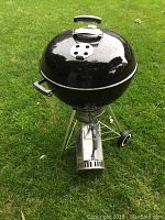 Full view front angle of Weber 22 inch charcoal kettle grill on grass with chimney attachment and wheels visible