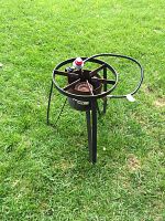 Photo showing single rusty metal propane burner with attached hose on grass