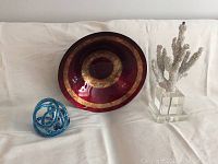Photo showing red and gold decorative bowl, blue glass decorative piece, and coral on acrylic stand displayed on white cloth.