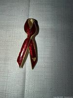 Front view of red enamel ribbon brooch with gold edging and heart detail