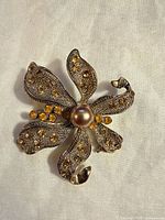 Front view of gold-tone floral brooch with amber rhinestones and central brown faux pearl