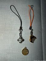 Two strap charms and one loose coin-style charm displayed on fabric