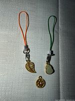 Two strap charms and a separate medallion charm displayed on fabric surface