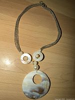 Full view of necklace showing shell pendant, faux pearls, gray bead strands