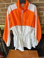 Full front view of orange and white Nike windbreaker on hanger