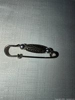 Overall view of silver-tone safety pin brooch with decorative center and beads