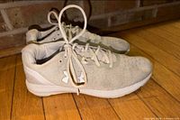 Side view of pair of white Under Armour sneakers on wooden floor