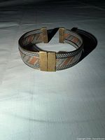 Top view of tri-color striped metal cuff bracelet showing hinged clasp and striped design