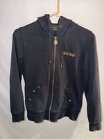 Front view of black gold zip hoodie jacket hanging