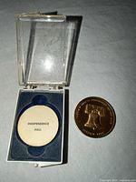 Coin next to open plastic display case showing felt insert and Independence Hall label