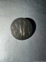 Front of silver monogram brooch showing engraved initials