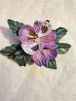 Front view of painted wooden pansy brooch with green leaves