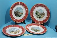 Four crimson rim plates with different scenes displayed upright and flat