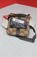 Front view of Coach crossbody bag, black floral paper tag visible, ivory pouch underneath