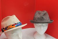 Both fedora hats on display heads, beige on left gray on right