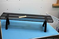 Oblique view of rectangular perforated black metal shelf on blue surface