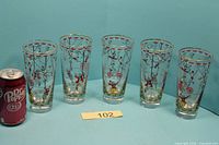 Five circus-illustrated gold-rim glasses next to soda can for scale