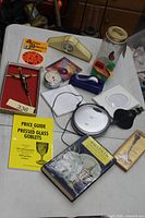 Full lot overview on table showing books, CD player, crucifix, jar, clocks and accessories