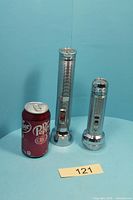 Two chrome flashlights beside soda can for scale