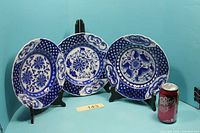 Three flow blue plates on stands beside soda can for scale