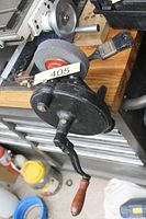 Overall view of hand-crank bench grinder mounted on workbench showing crank handle and wheel