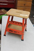 Full view of orange steel framed step stool with wood top