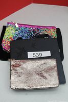 Four purses stacked showing metallic, satin, sequin and black surfaces