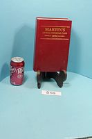 Front view of the red hardcover book standing beside a soda can for scale