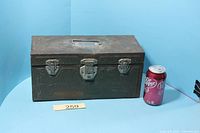 Closed green steel toolbox beside soda can for scale