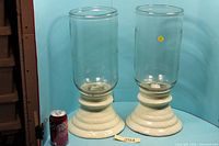 Pair of large glass hurricane candle holders beside soda can for scale