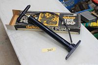 Pump placed atop open box showing cylinder, handle, hose, and interior of box