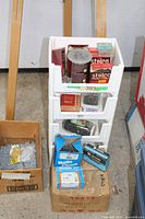 White plastic rack holding multiple boxes, jars and cans of nails plus adjacent boxes