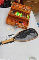 Tackle box open with lures, pliers, bobber and hand net shown