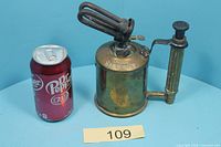 Full view of brass blow torch beside soda can for scale