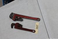 Two red pipe wrenches on table, size comparison