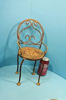 Front view of miniature wrought-iron chair next to soda can for scale