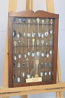 Full view of wood rack with glass front holding souvenir spoons