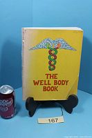 Front cover of The Well Body Book next to soda can for scale
