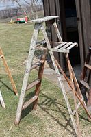 Side view of the wooden step ladder opened on grass showing rungs, braces and paint wear