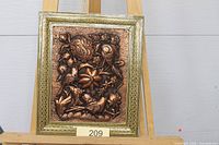 Full view of framed copper repoussé wall plaque on easel