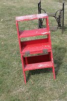 Front view of red wooden folding chair in ladder position showing three steps and hinges