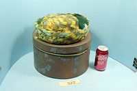 Hat resting atop matching hat box beside soda can for scale