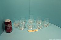 Front view of eight clear etched juice glasses beside soda can for scale