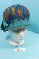 Front view of feather hat on mannequin showing veil and feather colors