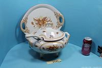 Complete tureen set with platter and ladle beside soda can for scale