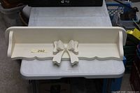 Front angled view of cream wood shelf showing bow detail